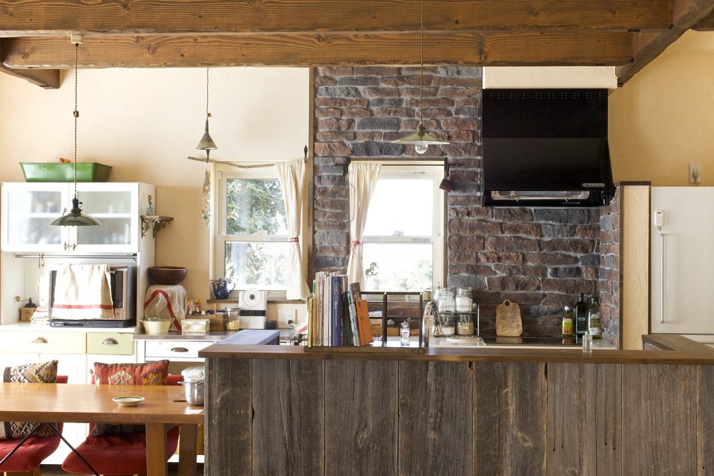 アンティークの食器棚とよく似合う、古材とレンガを組み合わせた手作り感あるオープンキッチン。